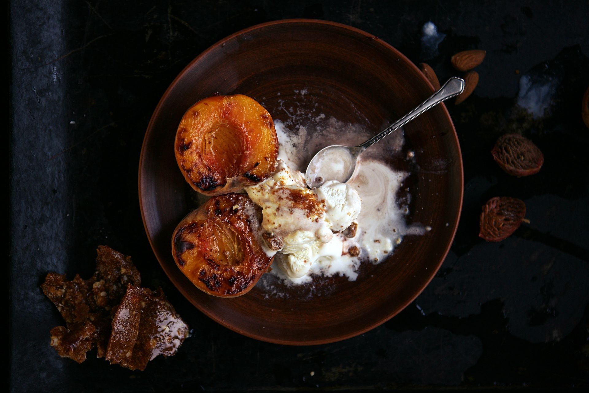 Roasted peaches with vanilla ice cream on a brown plate, dark background.