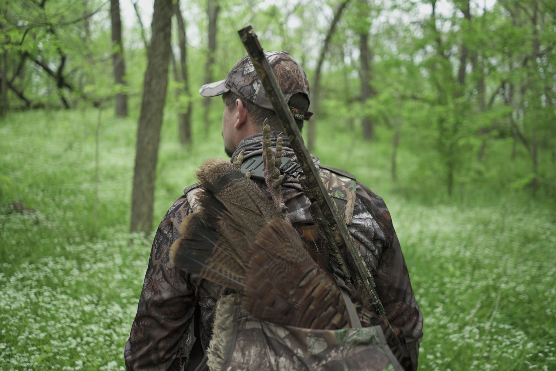 man hunting in the woods with a rifle and a turkey in his bag.