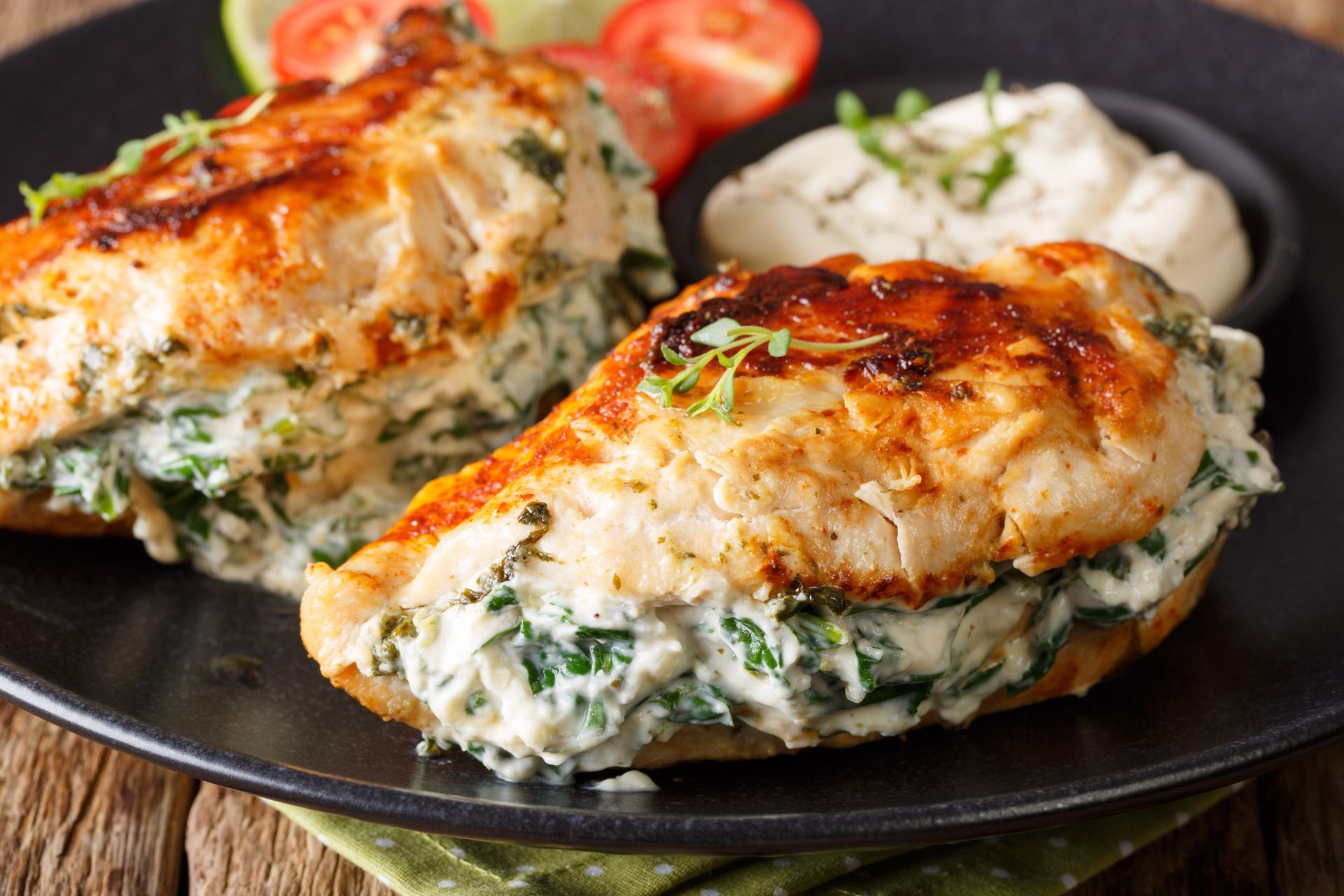 Stuffed chicken breast with spinach and creamy filling, served on a black plate with garnish.