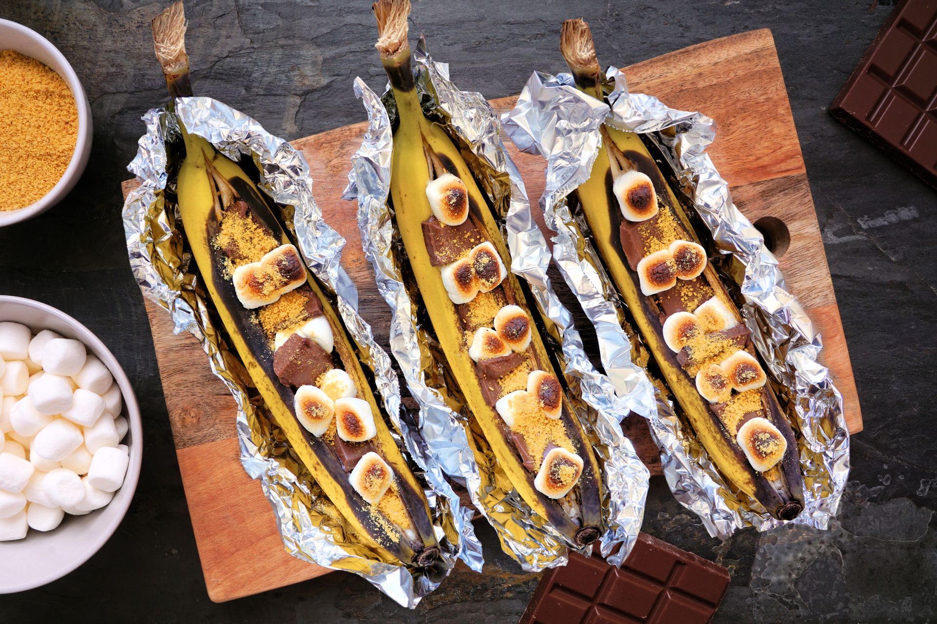 Grilled banana boats with marshmallows and chocolate on a wooden board.