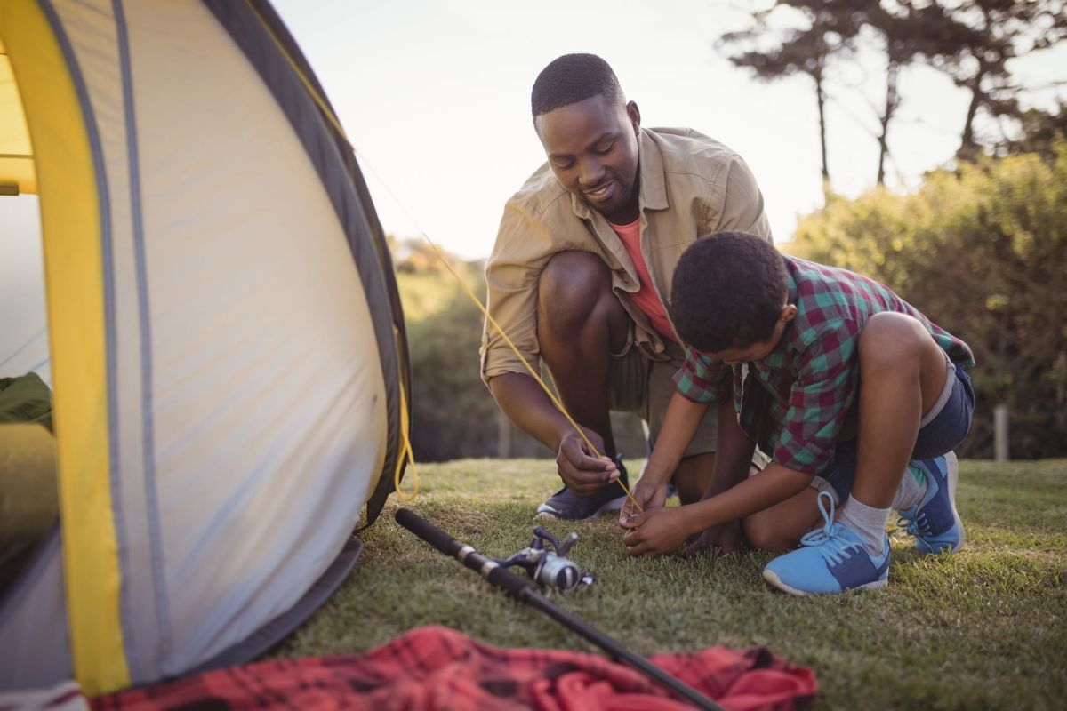 A man and a boy are setting up a tent in the grass.