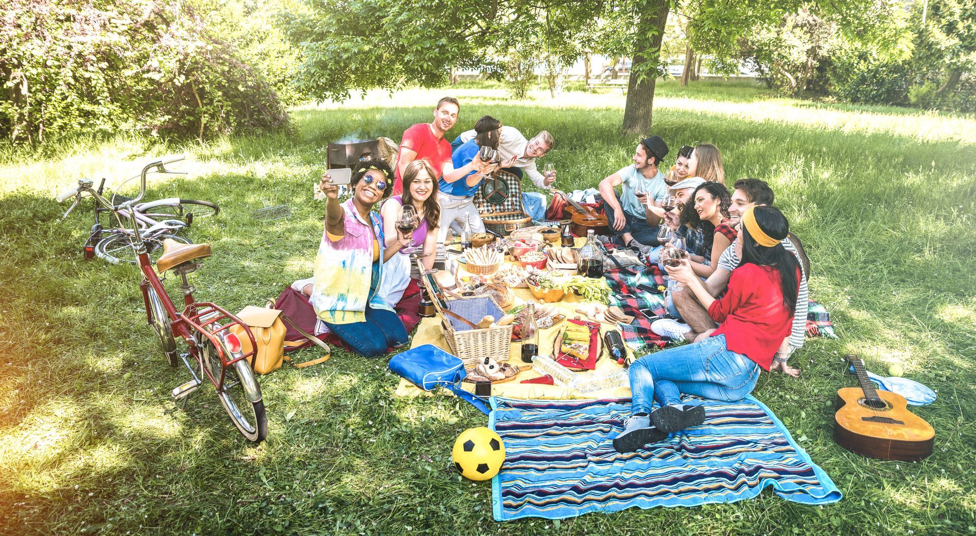 Group of friends having a picnic in a park, sitting on a blanket, enjoying food and music.