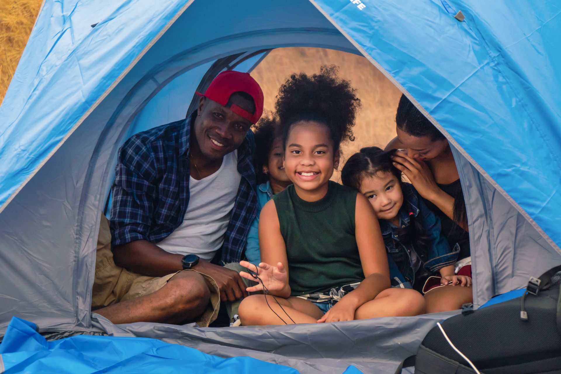 A family sits smiling together inside a blue tent while camping.