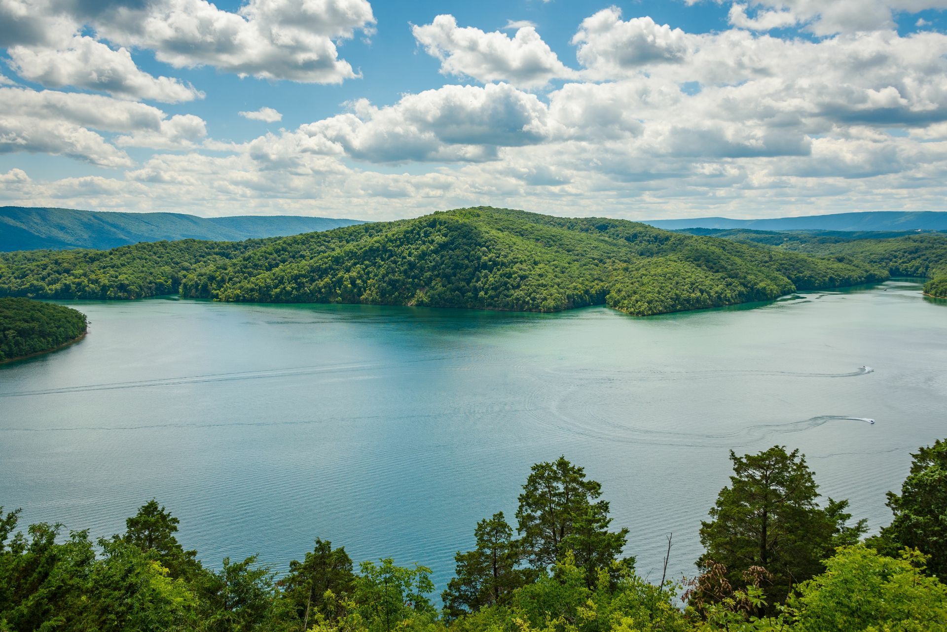 A large lake surrounded by mountains and trees on a cloudy day.