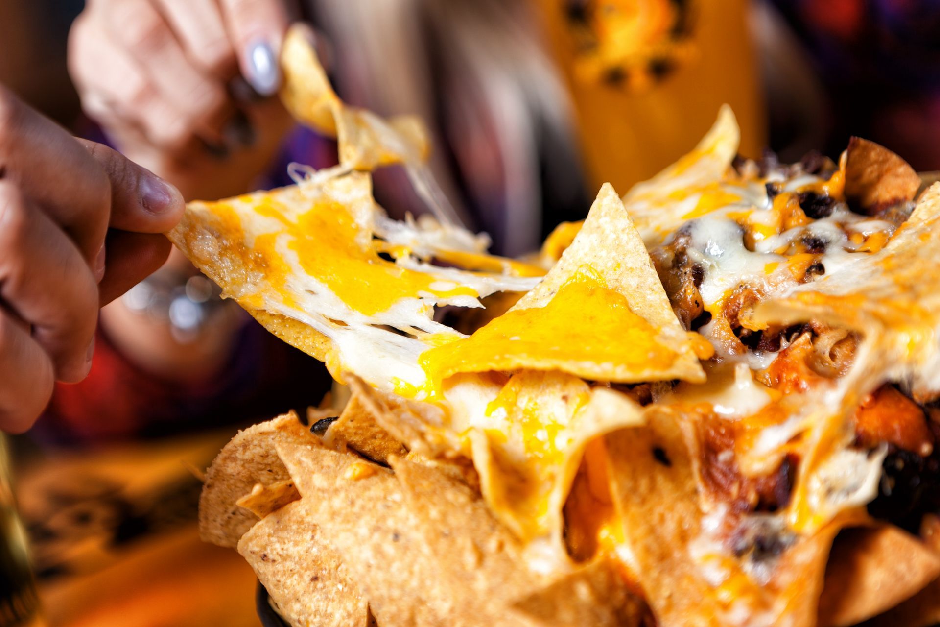 Person pulling cheesy nachos apart; melted cheese, chips, and toppings visible.