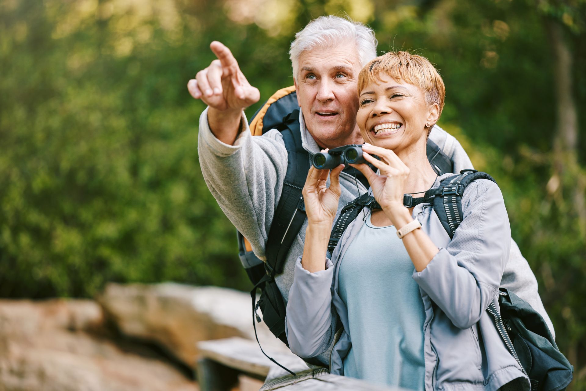 Couple hiking, woman with binoculars, man points, outdoors.
