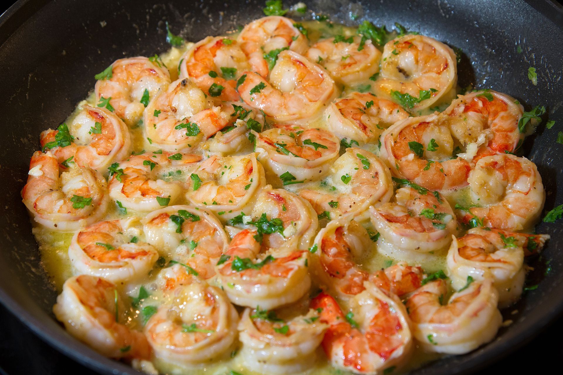 Shrimp sautéing in a pan with garlic and parsley.