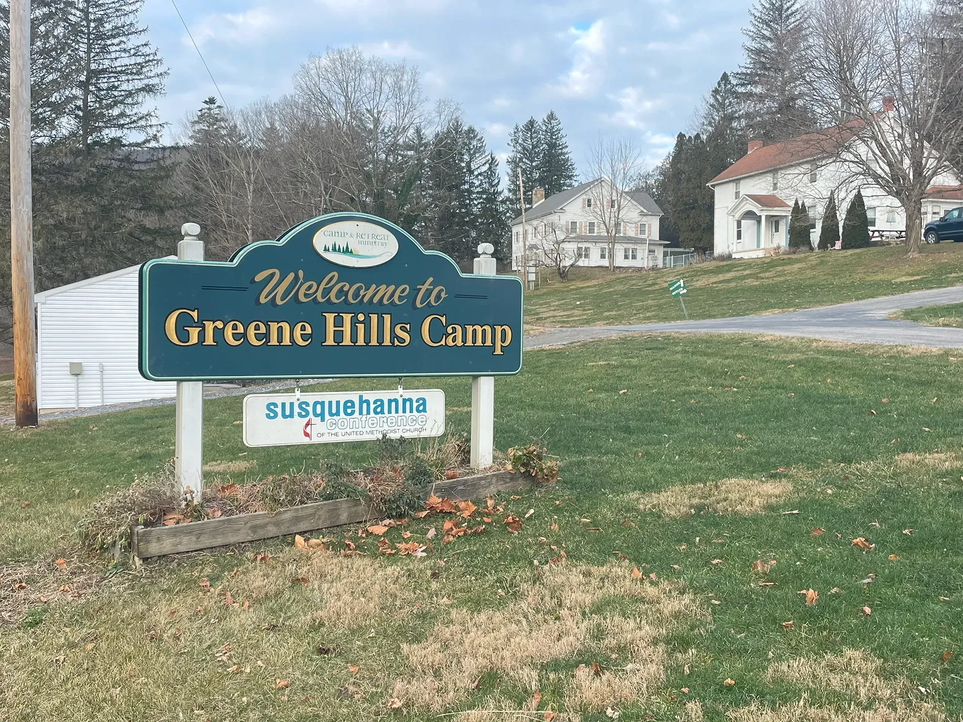 A welcome to greene hills camp sign is in the middle of a grassy field.