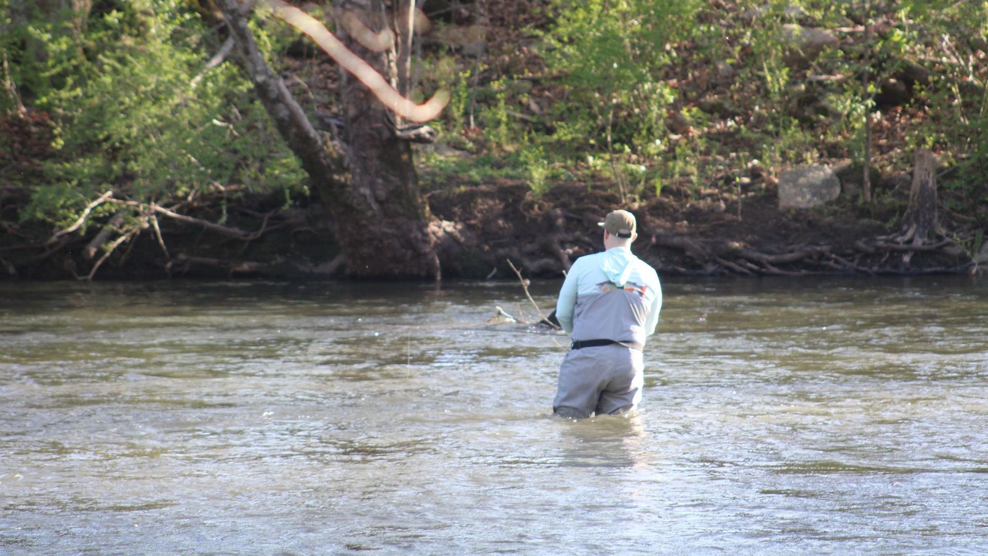 A man is fishing in a river with a fishing rod.