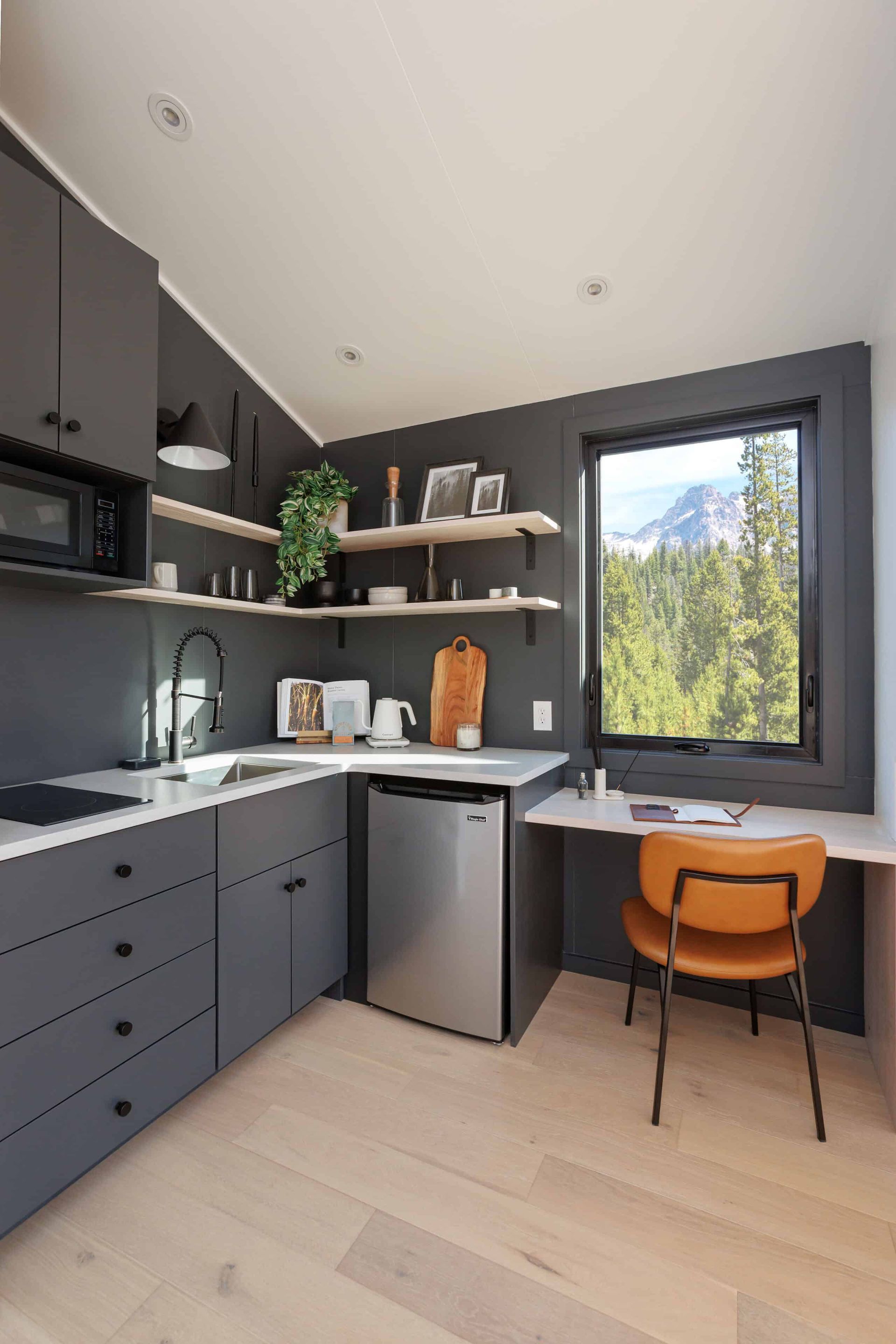 A kitchen with gray cabinets , a stainless steel refrigerator , a sink , a desk and a window.