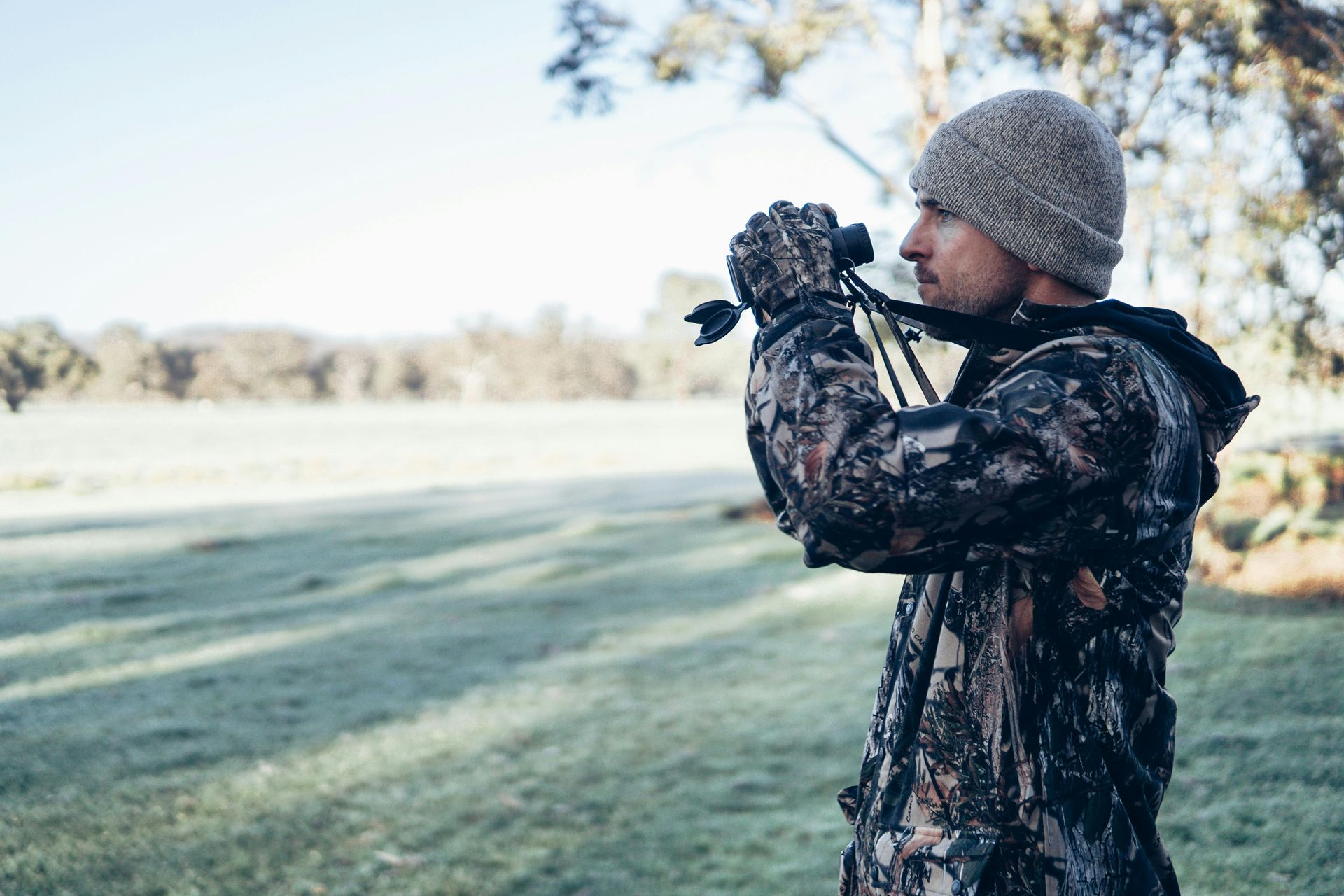 A man is looking through binoculars in a field.