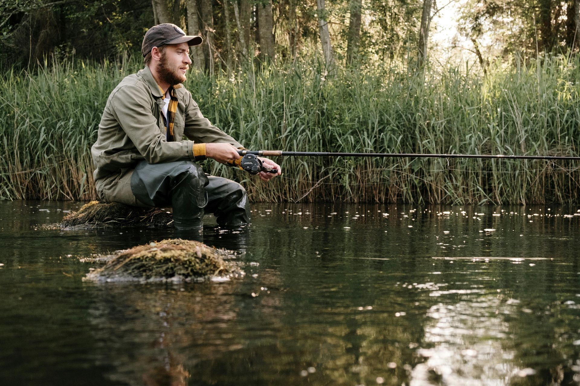 A man is sitting on a rock in the water holding a fishing rod.