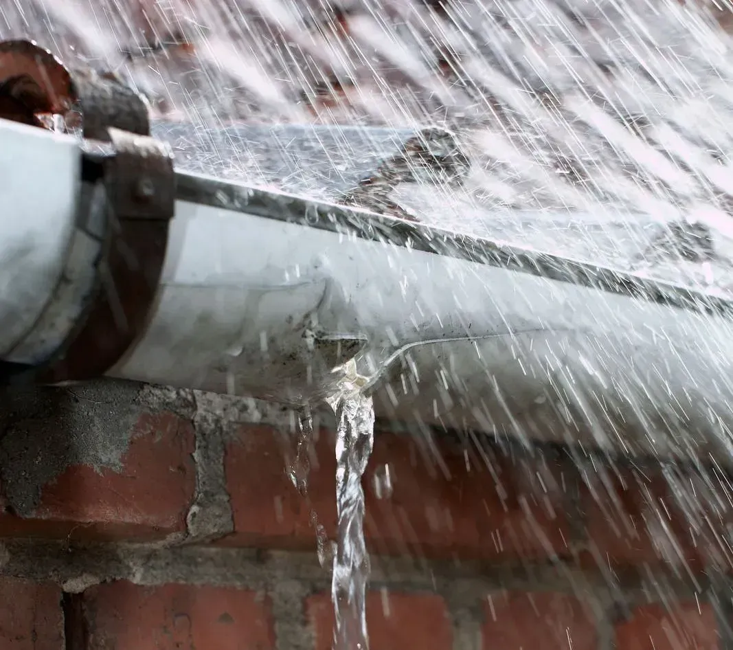 Water is coming out of a gutter on a brick wall.