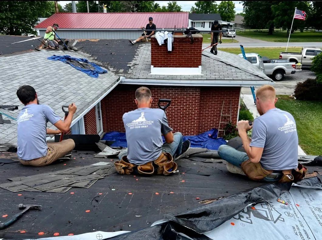 Roofers working on a residential roof, removing old shingles and preparing for replacement.