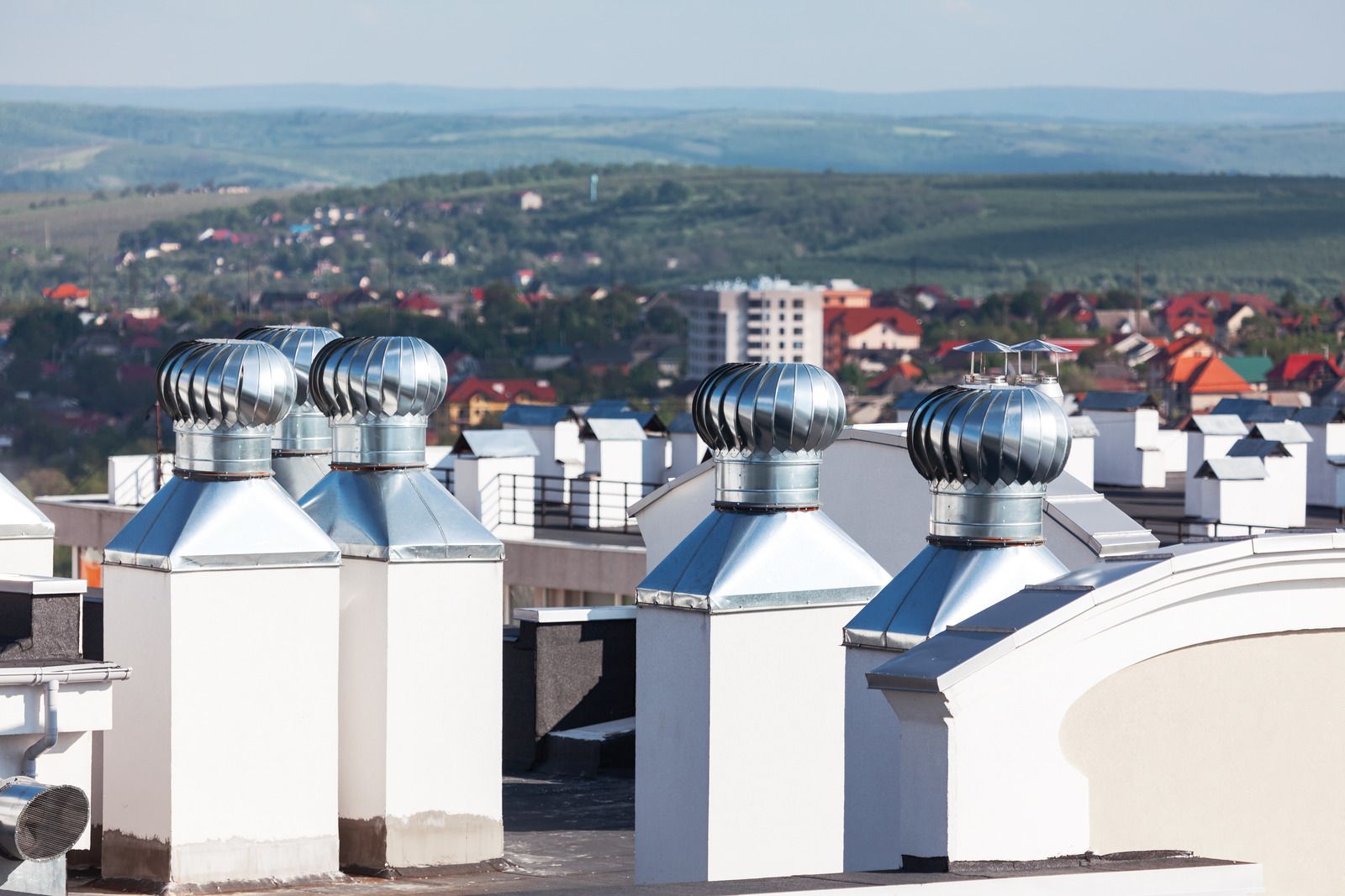 Rooftop vents with rounded metal tops against a distant cityscape with green hills and colorful buildings.