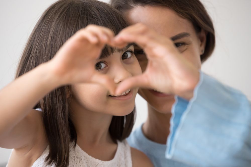 Girl and woman making heart shape with hands, smiling at camera.