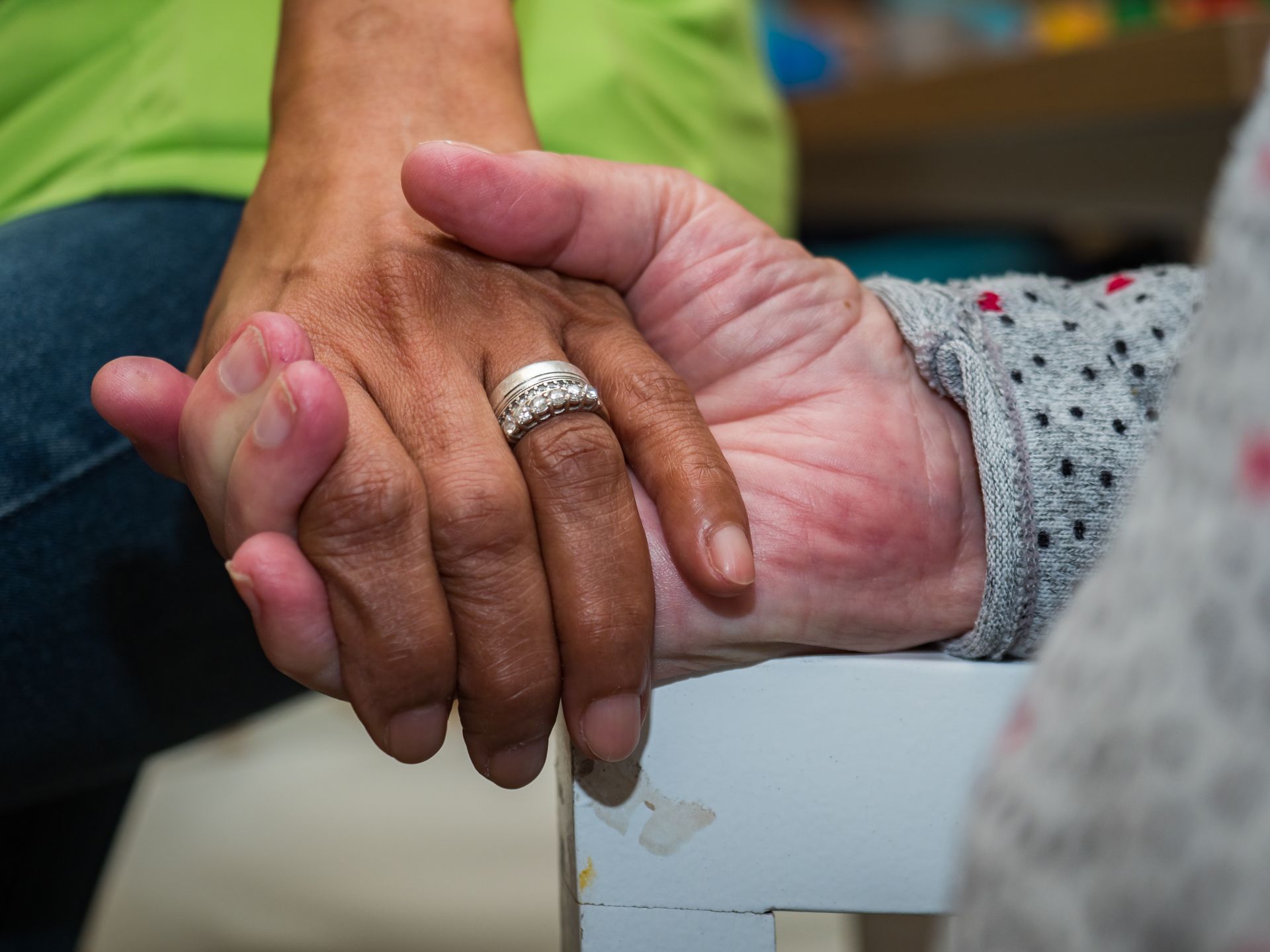 Nurse in blue scrubs holds patient's hands, offering comfort. A stethoscope hangs around the nurse's neck.