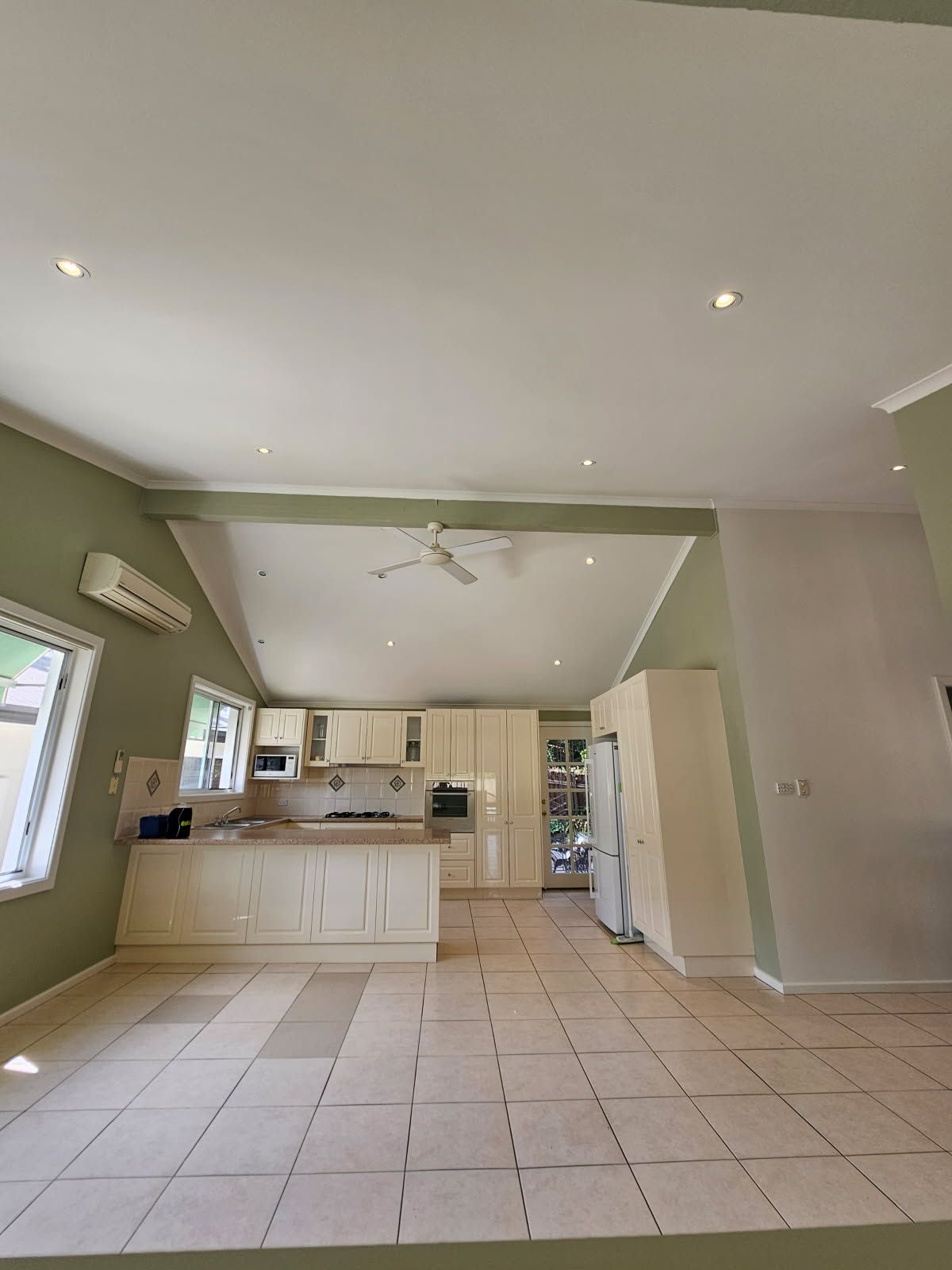 A kitchen with white cabinets , a refrigerator , and a ceiling fan.