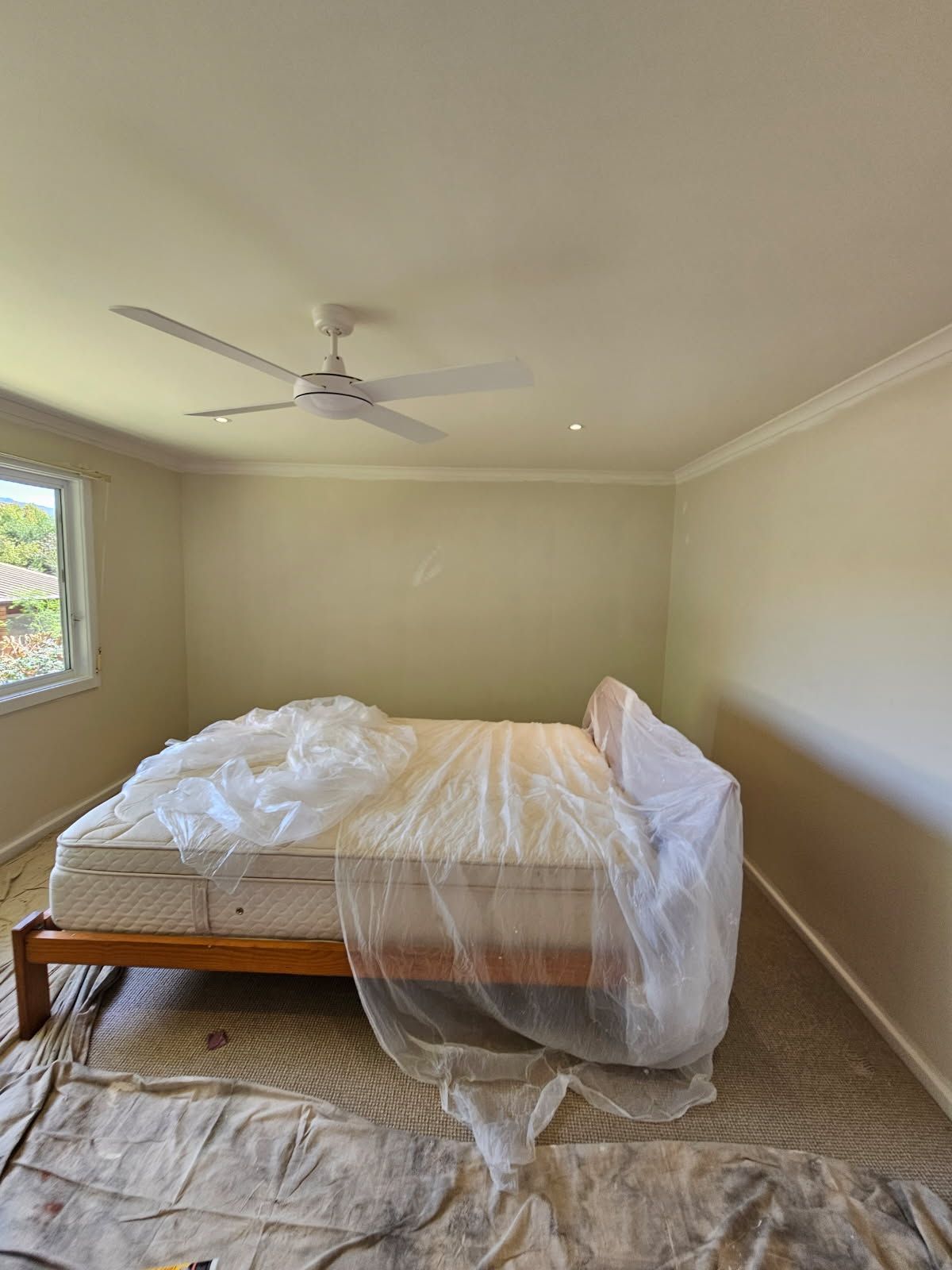 A bedroom with a bed and a ceiling fan covered in plastic.