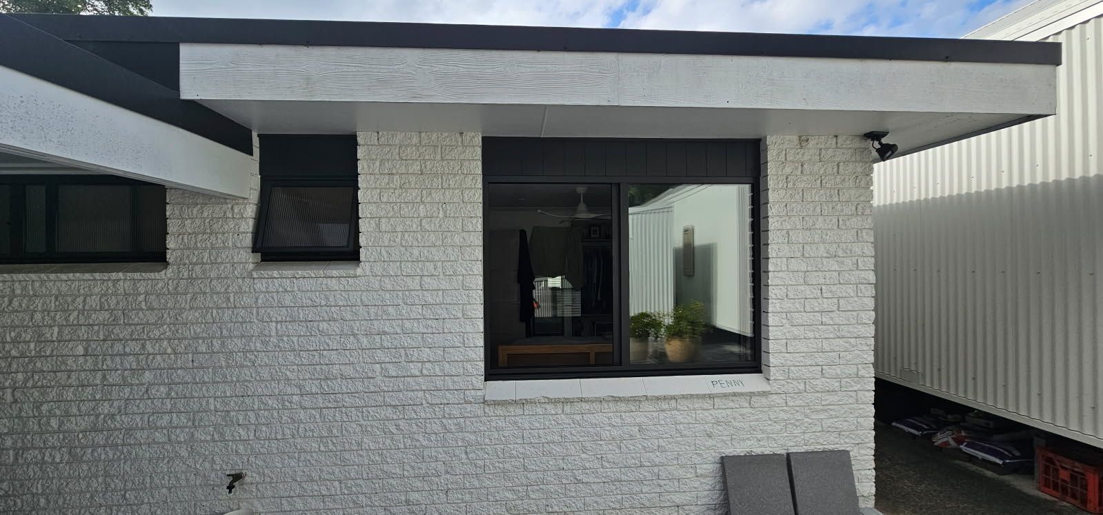 A white brick house with a large window and a black roof.