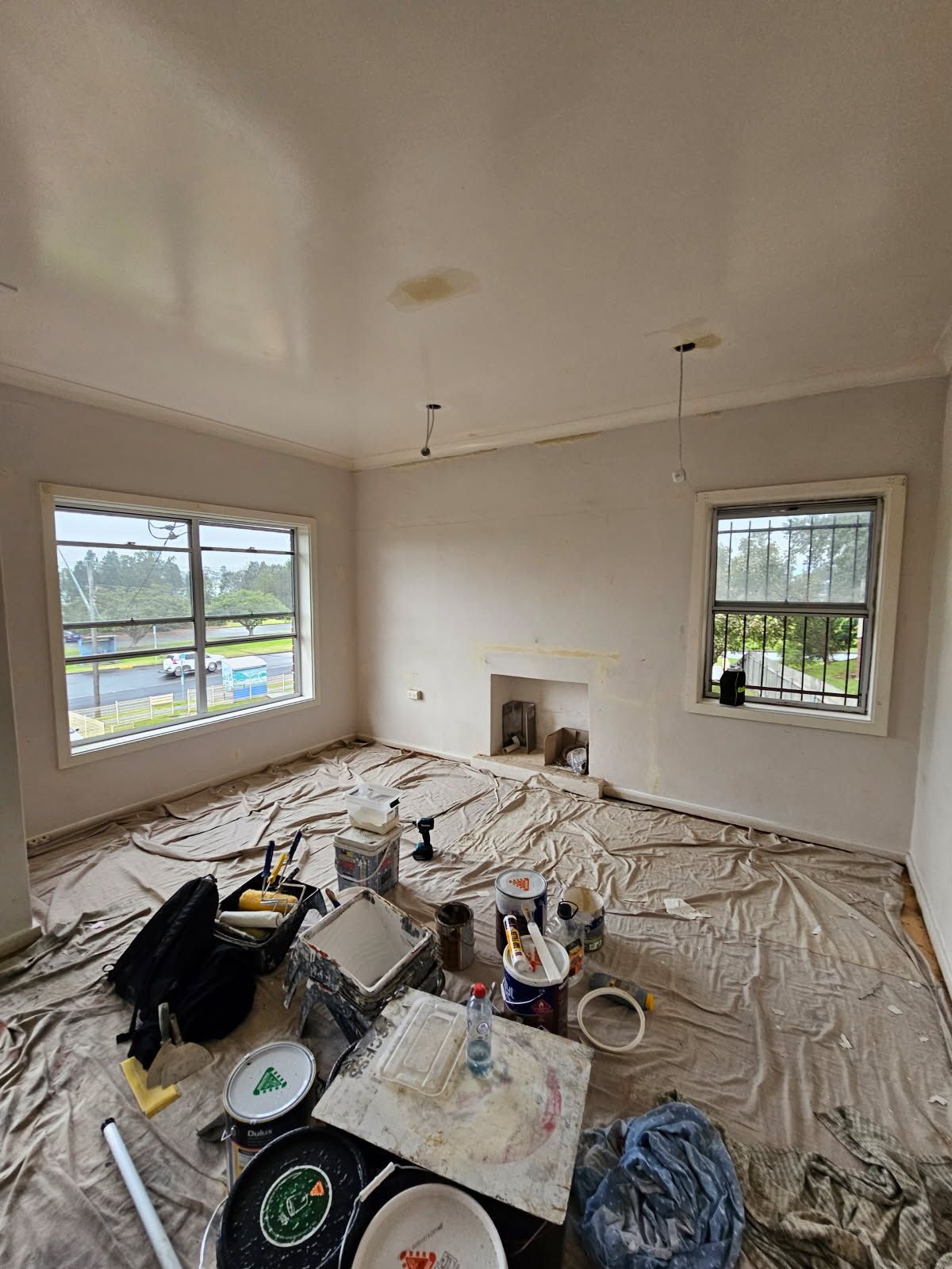 A living room is being painted and there is a lot of paint on the floor.