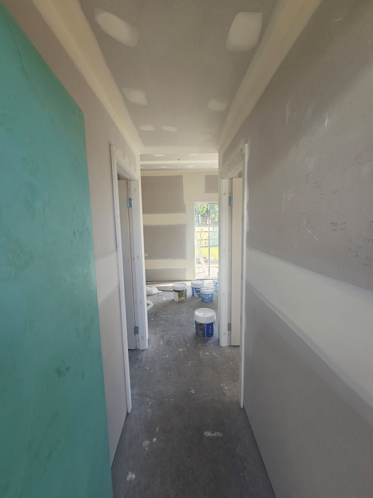 A long hallway with drywall on the walls and a window.