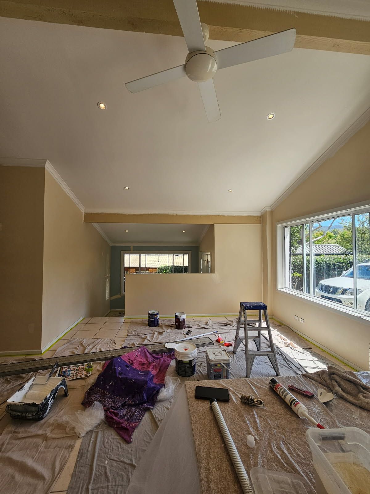 A living room is being painted with a ceiling fan.
