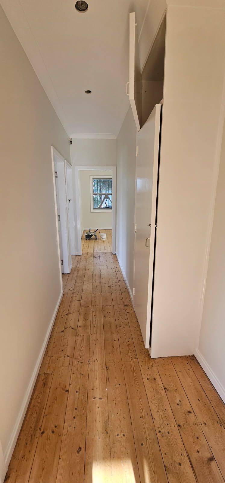 A long hallway with wooden floors and white walls in a house.