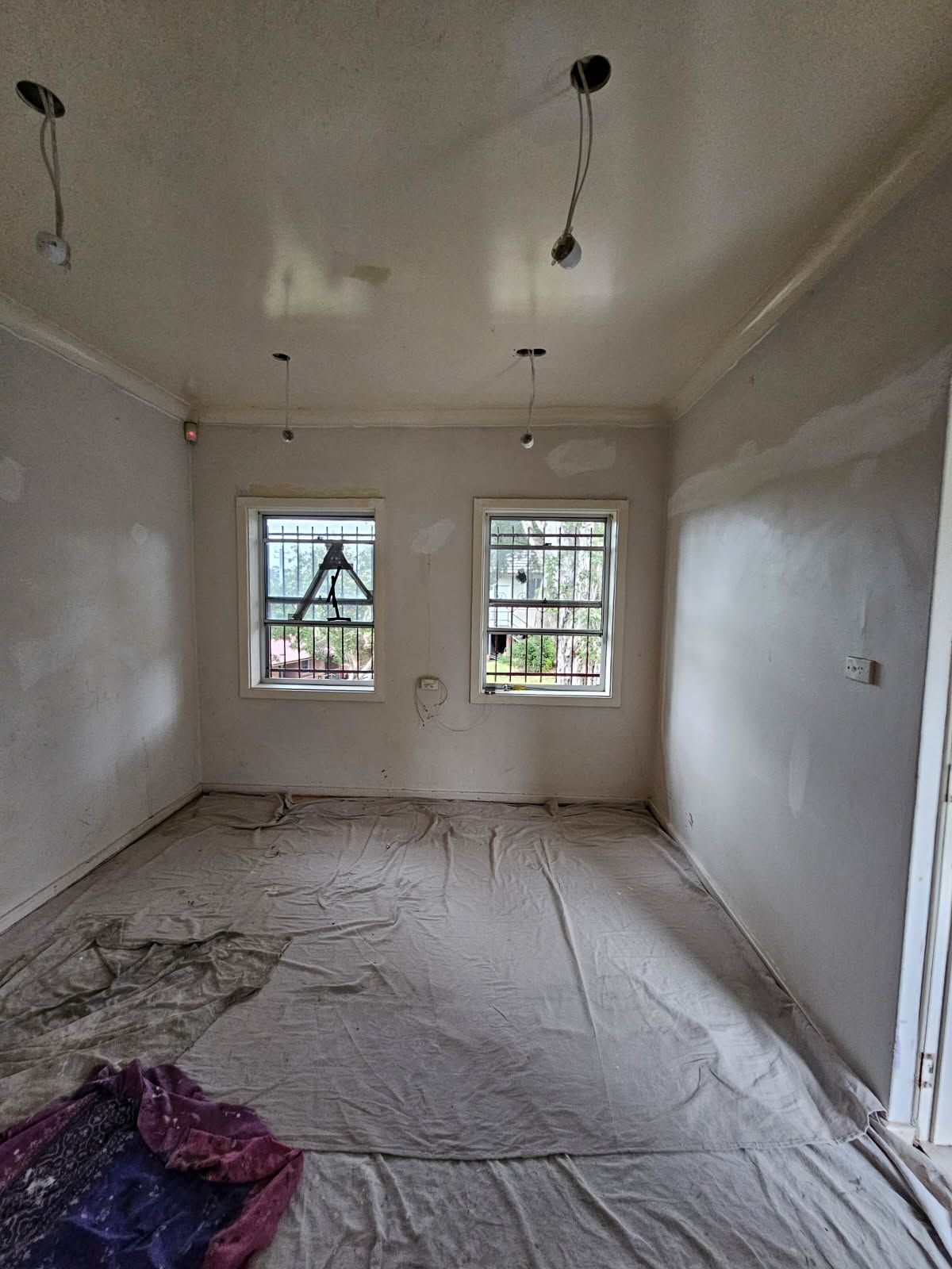 An empty room with a blanket on the floor and two windows.