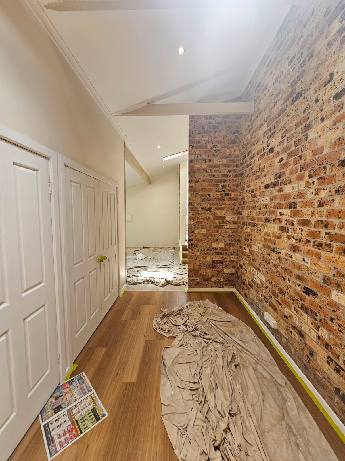 A hallway with a brick wall and a sheet of paint on the floor.