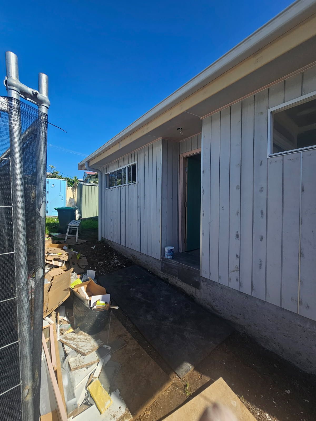 A white house with a green door is being built next to a chain link fence.