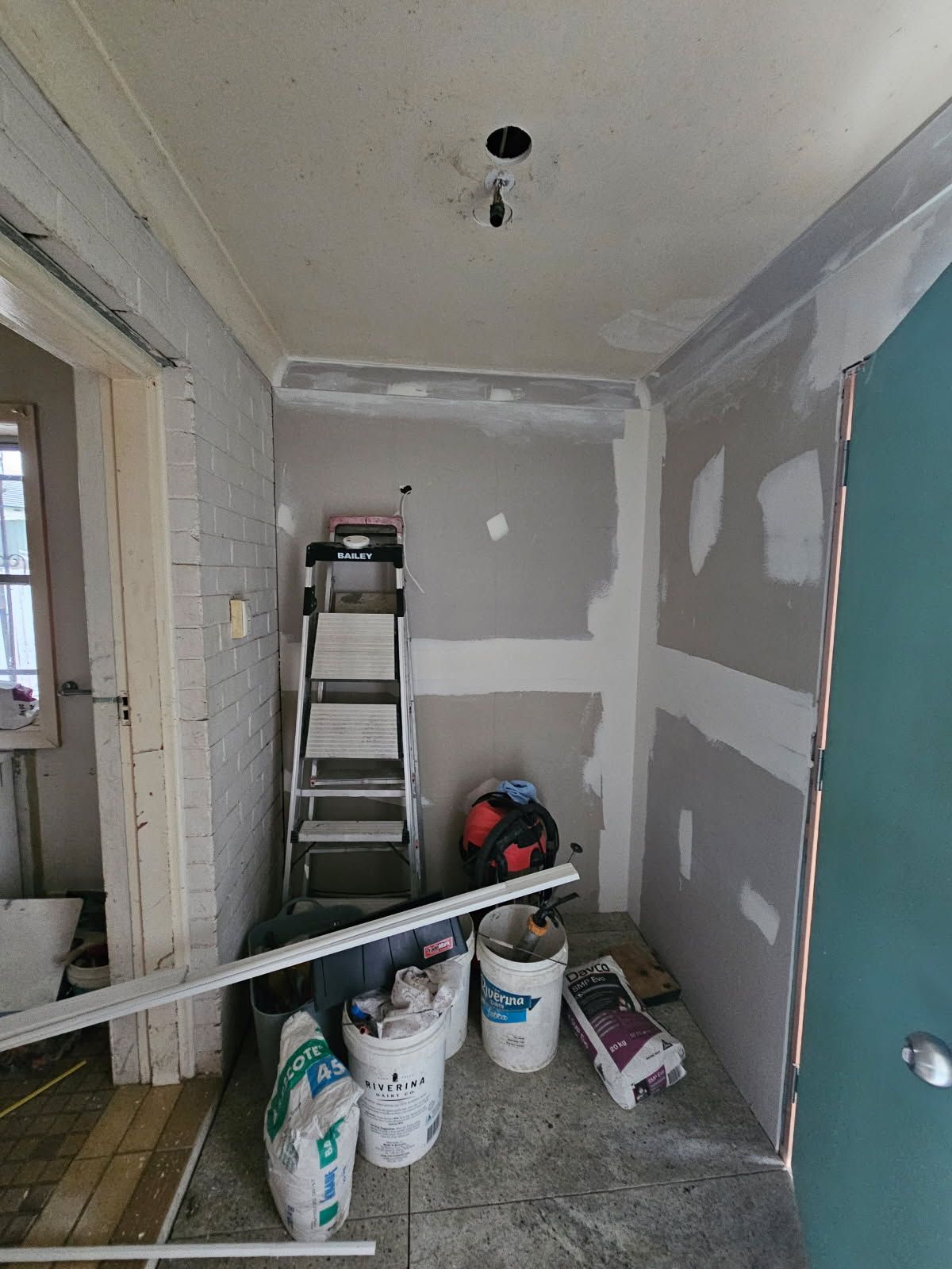 A room with buckets of paint and a ladder in it.