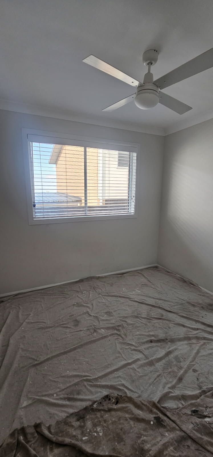 An empty room with a ceiling fan and a window.