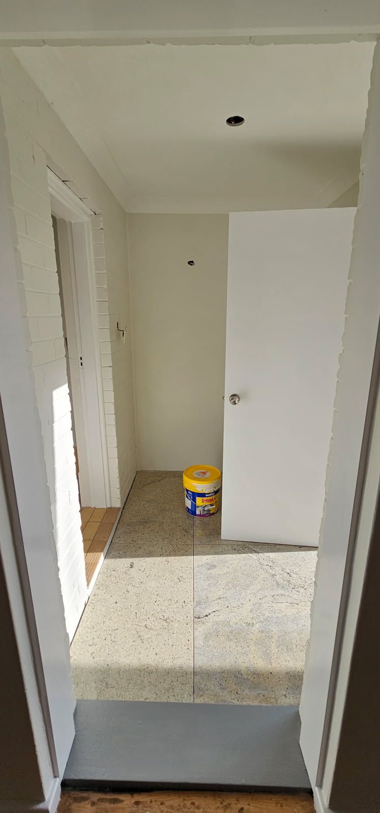 A room with a door and a bucket of paint on the floor.