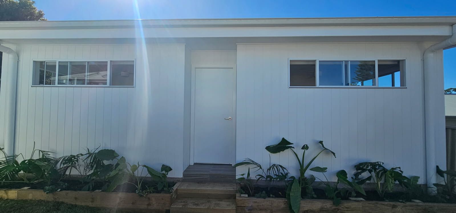 A white house with a lot of windows and plants in front of it.