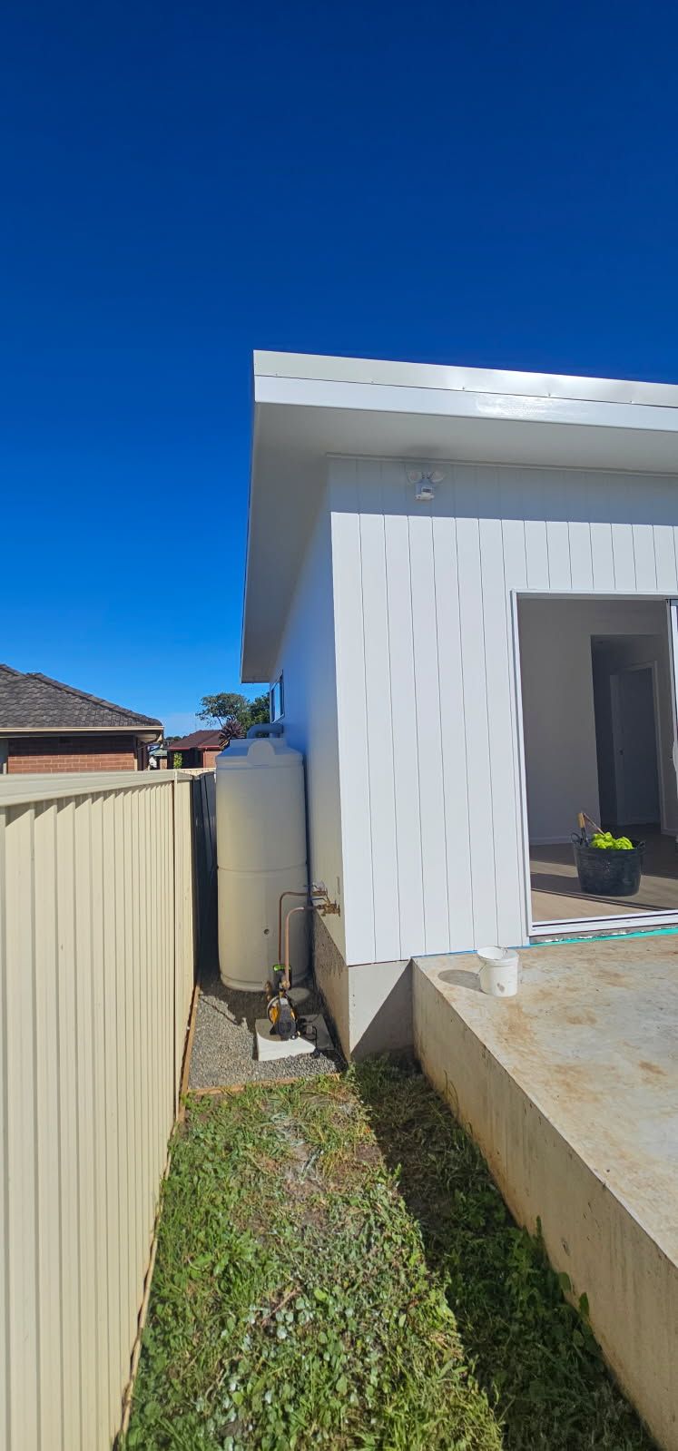 A white house with a water tank in the backyard next to a fence.