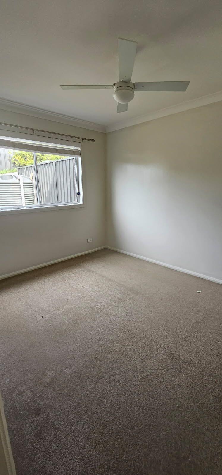 An empty room with a ceiling fan and a window.