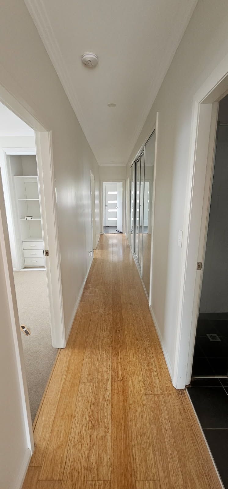 A long hallway with wooden floors and white walls in a house.