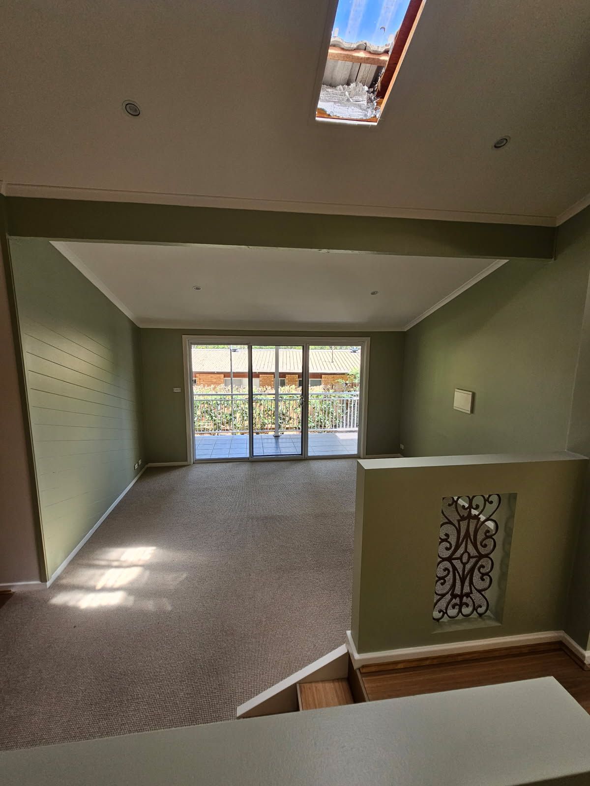 An empty living room with a skylight and sliding glass doors.