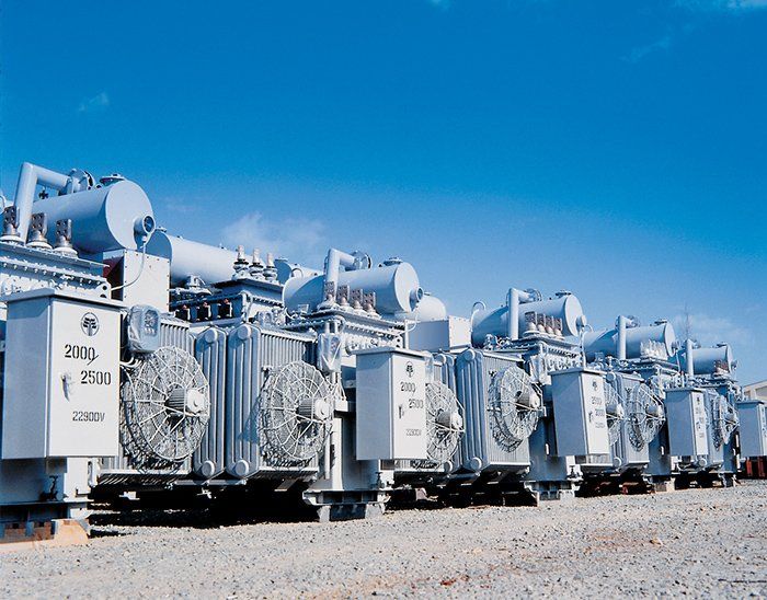 A row of transformers are lined up in a dirt field. Drives and Motors