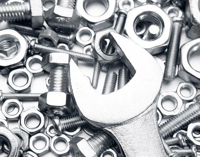 A wrench is sitting on top of a pile of nuts and bolts.
