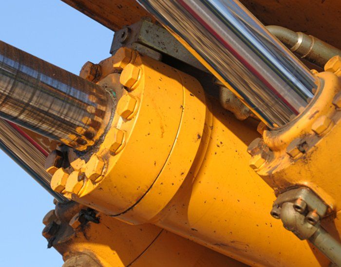 A close up of a yellow hydraulic cylinder with a blue sky in the background