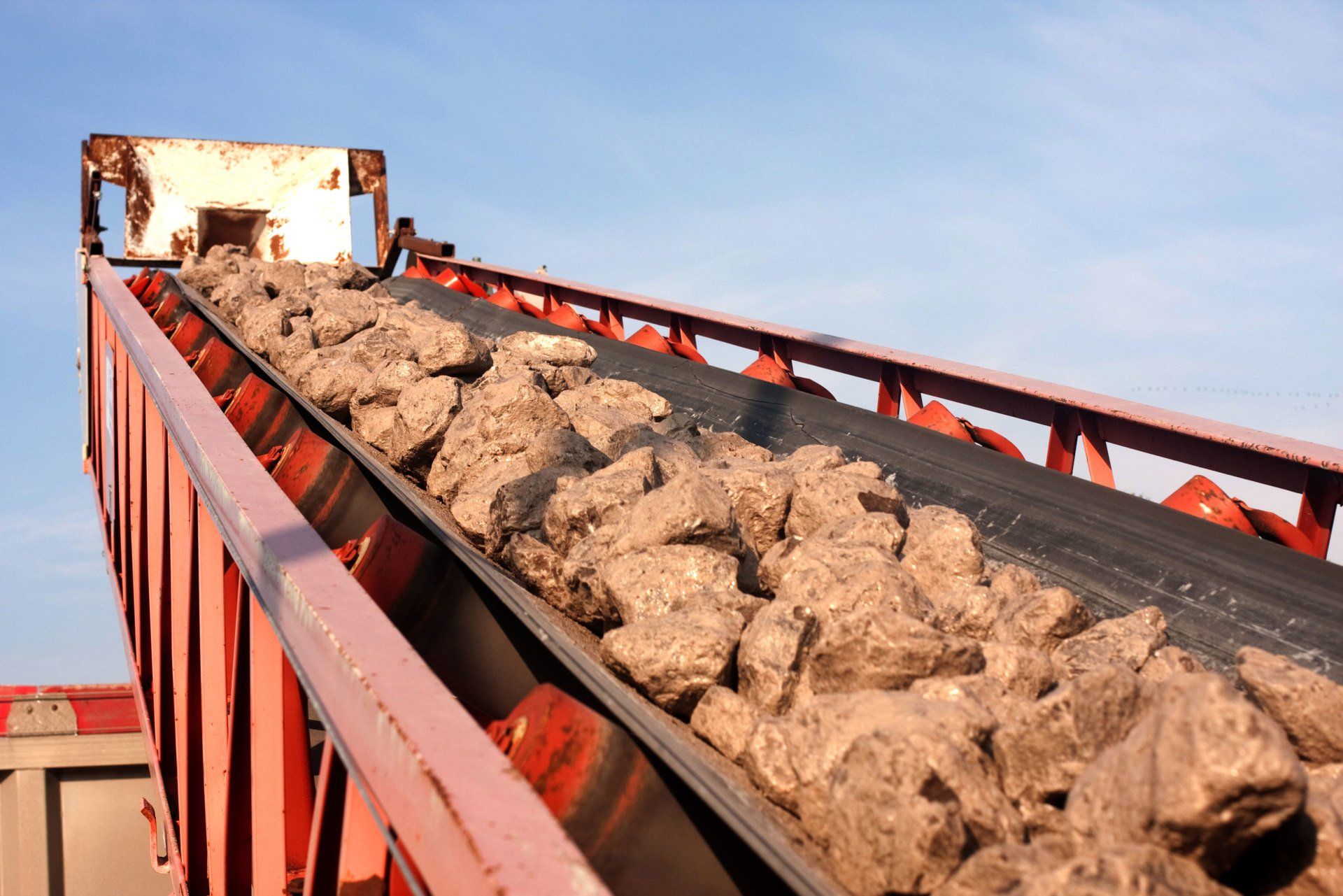 A conveyor belt filled with rocks is going down a hill.