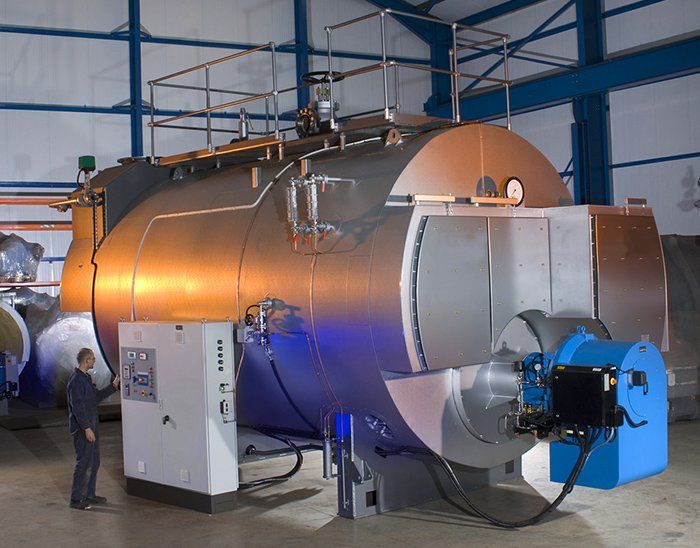 A man is standing in front of a large machine with a blue burner