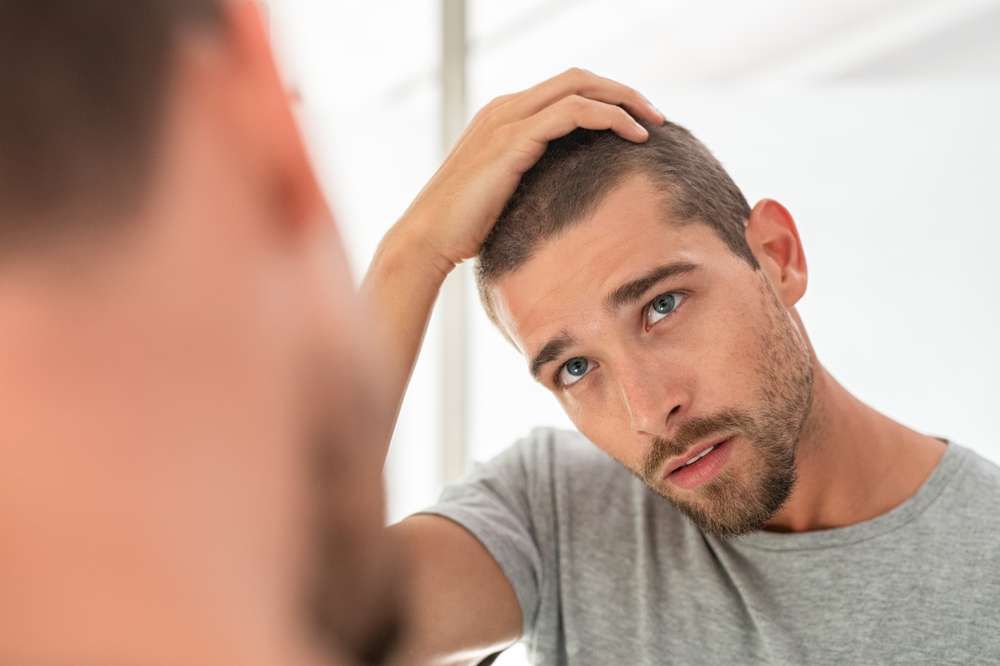 A man is looking at his hair in the mirror.