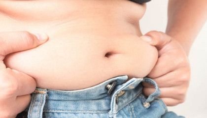 A person is holding their stomach with their hands while wearing jeans.