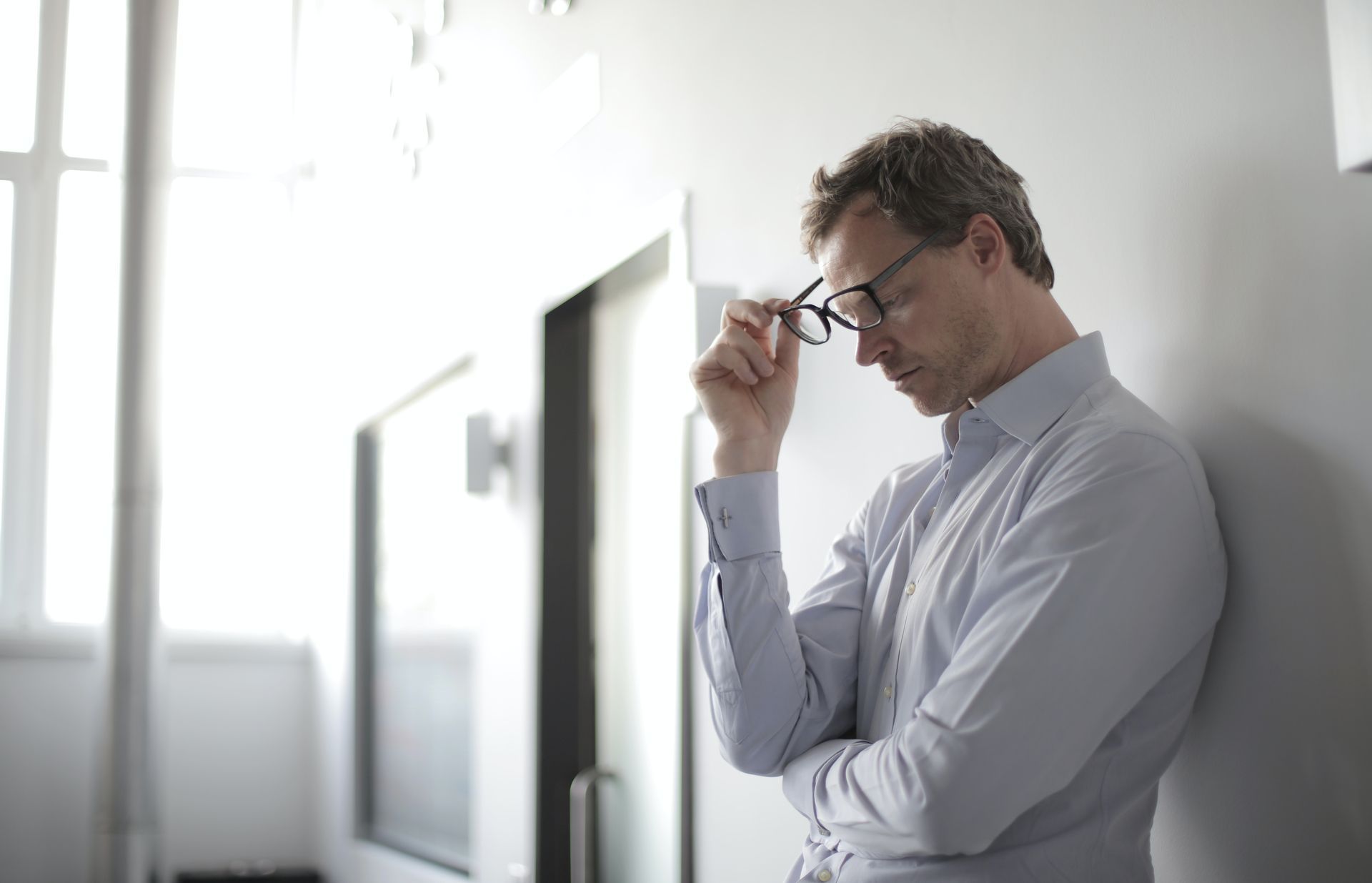 A man wearing glasses is leaning against a wall.