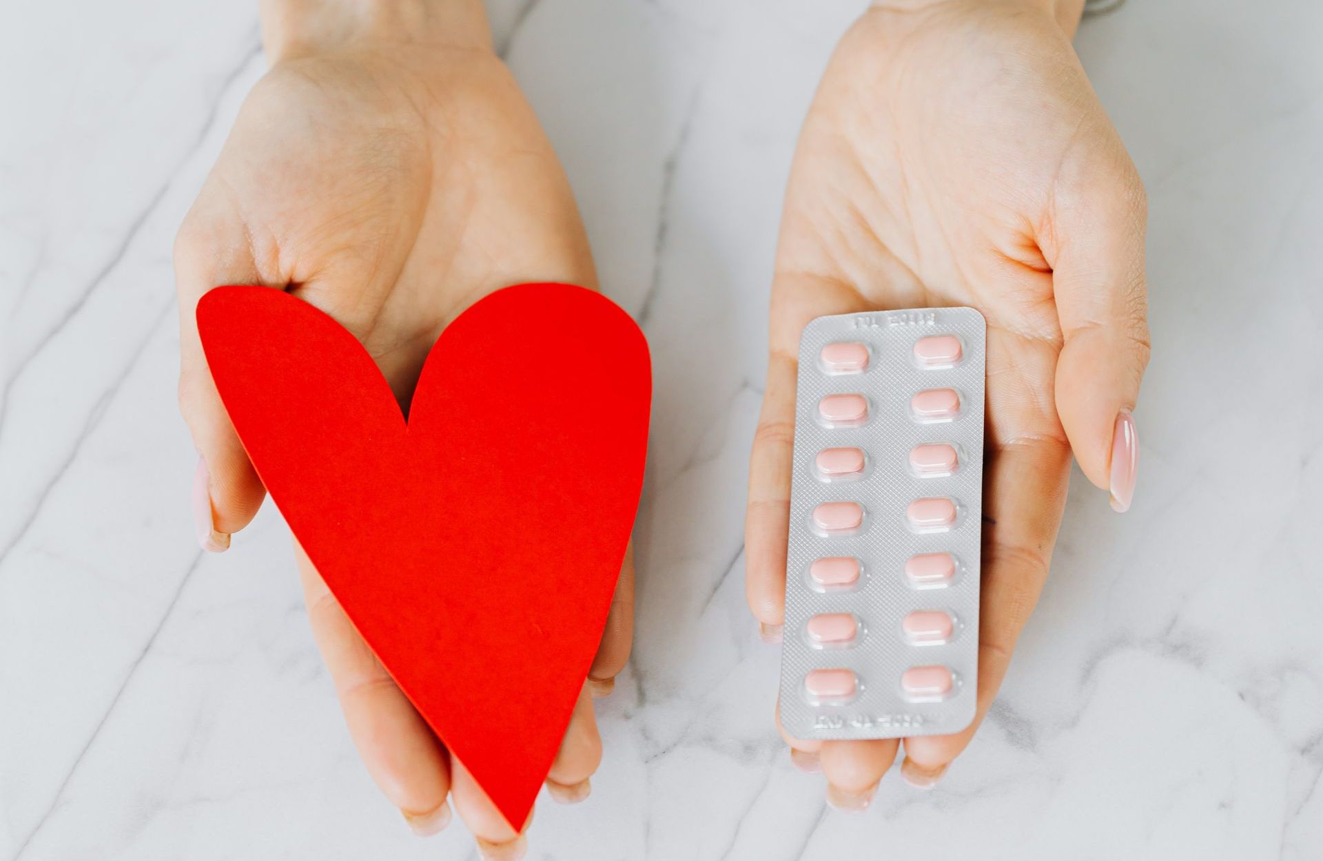 A woman is holding a red heart and a blister pack of pills.