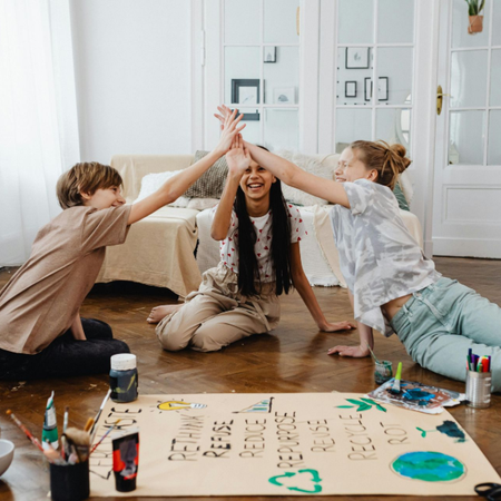 Young person with glasses smiles, sitting on a bed indoors.