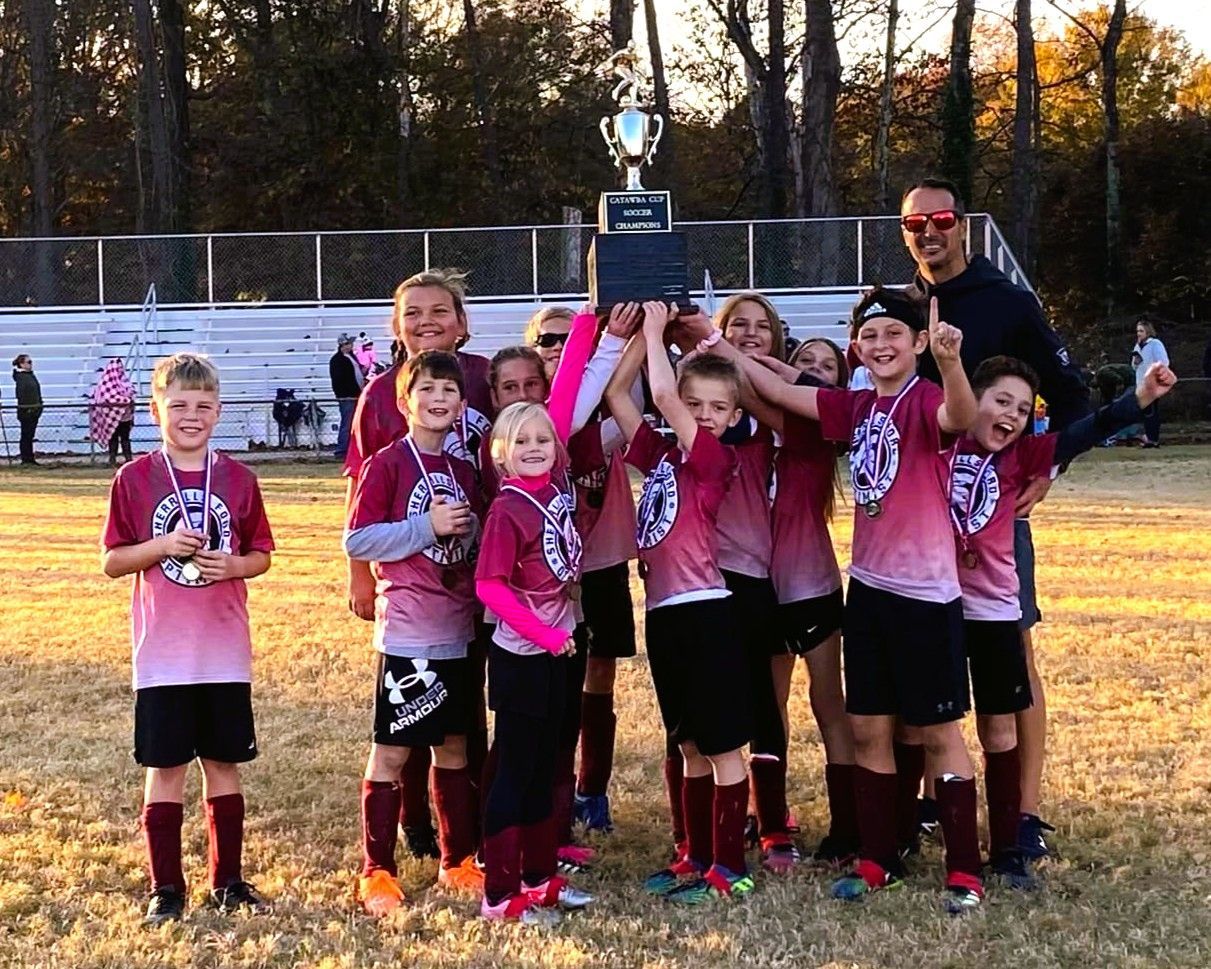 Youth soccer team holding trophy after winning game. Team is wearing burgundy and black. Smiling, excited.